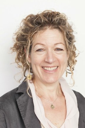 Headshot of a woman with curly blonde hair, smiling, wearing a dark blazer and a white blouse.
