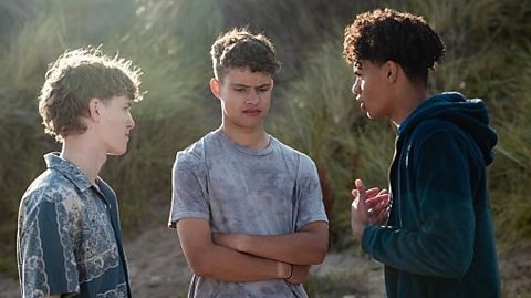 Five diverse teenagers sitting in a circle on grass playing cards and enjoying a sunny day.