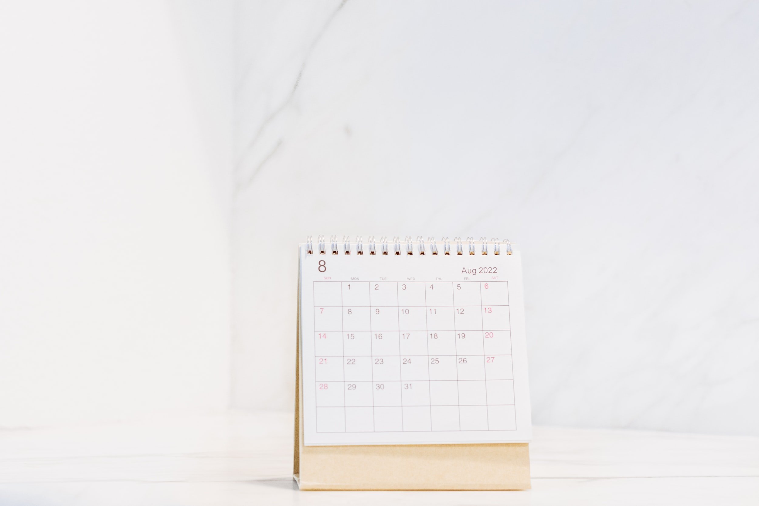 Desk calendar showing August 2022 on a white surface against a white wall.