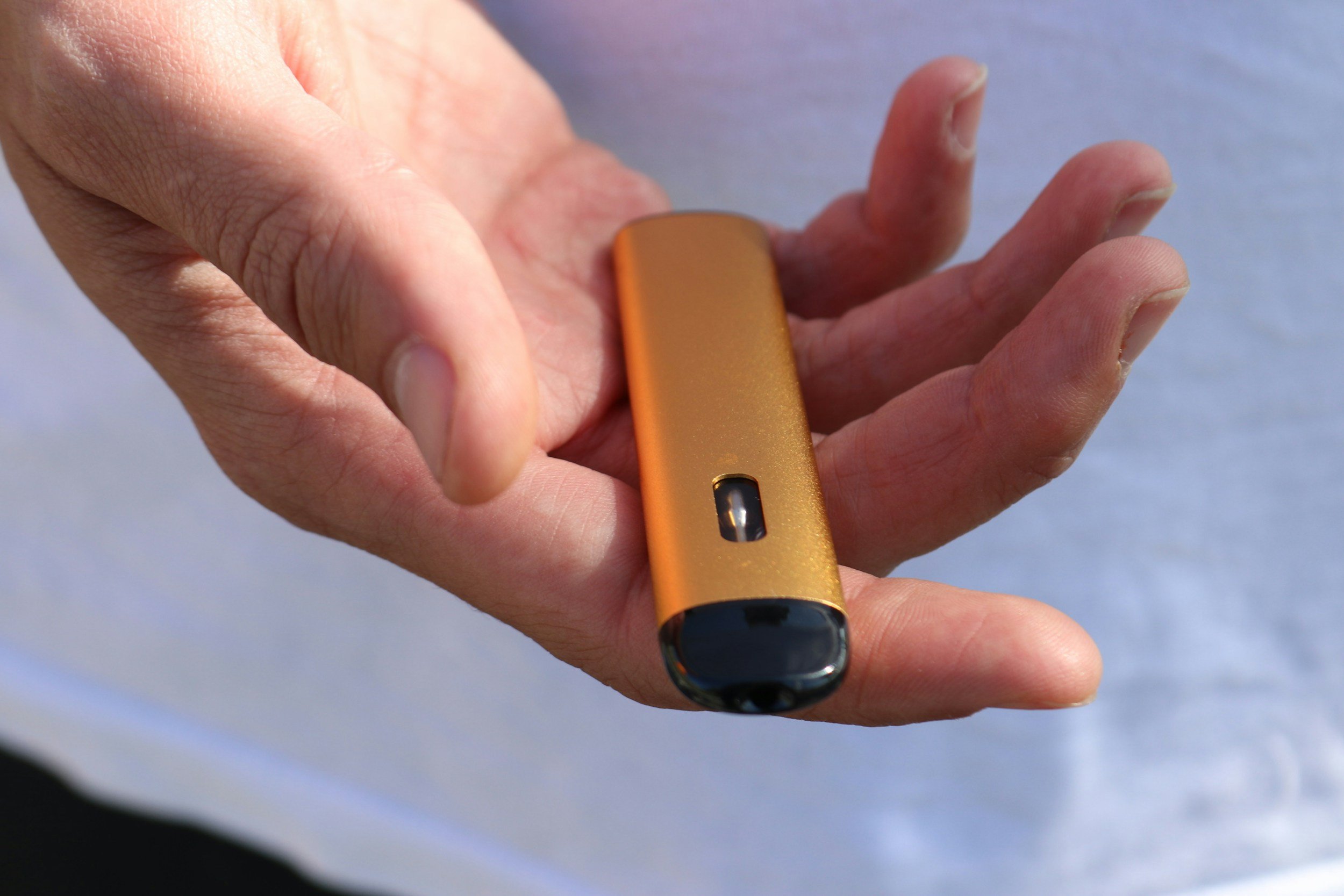 A hand holding an orange and black vape device.