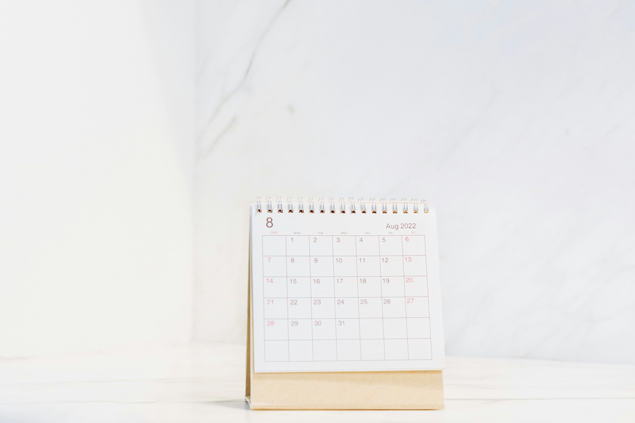 Desk calendar displaying August 2022, positioned on a plain white surface with a marble-textured wall in the background.