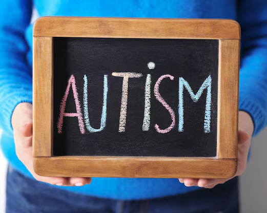 Person holding a small chalkboard with the word 'AUTISM' written in colorful chalk.