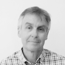 Black and white photo of a middle-aged man with gray hair, wearing a checkered shirt, looking at the camera with a neutral expression.